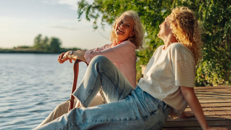 två seniora kvinnoe sitter vid vattnet och är glada.