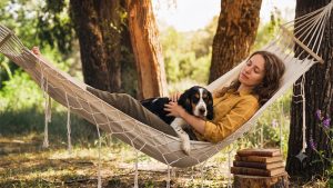 kvinna myser i hängmatta med sin hund. Foto: Gemini